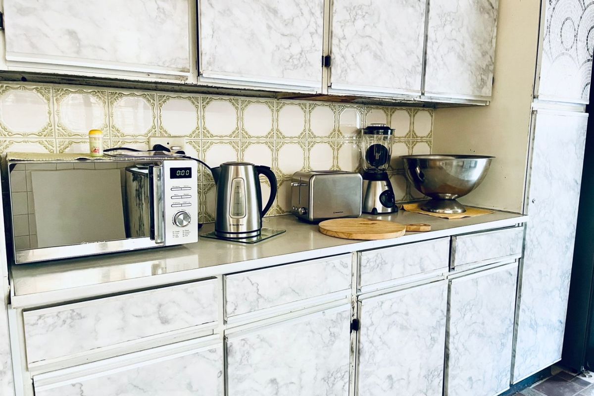 A functional kitchen area featuring marble-effect laminate cabinetry and a classic ceramic tile backsplash, offering a dated aesthetic ready for modernization.