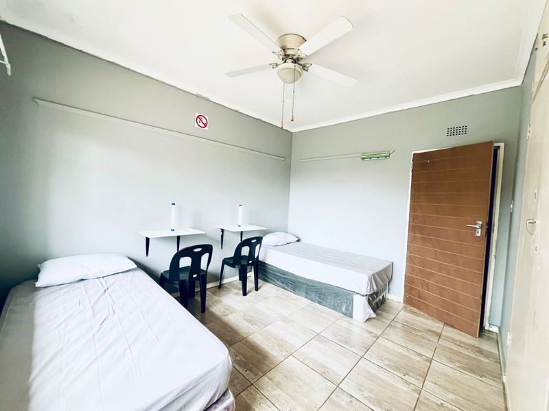 A functional bedroom featuring tiled flooring, a ceiling fan, and built-in wall shelving, providing a basic layout for sleeping or study.