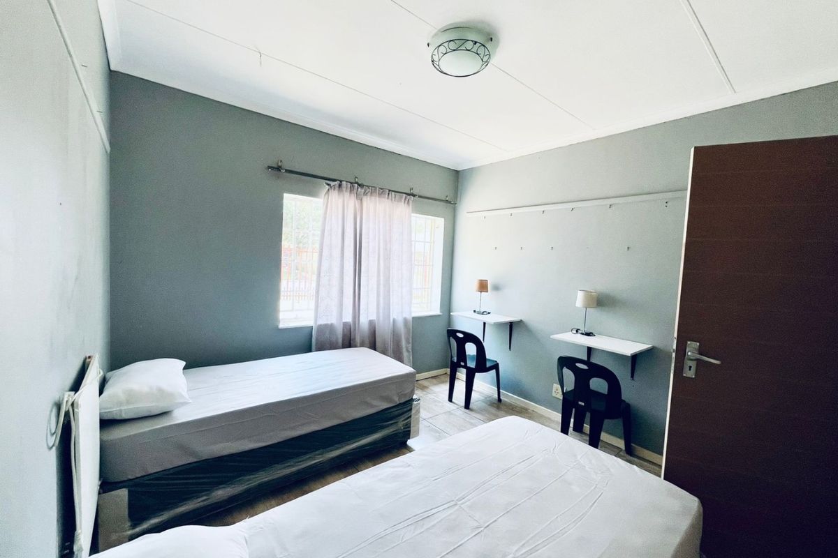 A functional bedroom featuring tiled flooring, built-in wall-mounted desks, and a window with security bars, offering a practical space for residents.