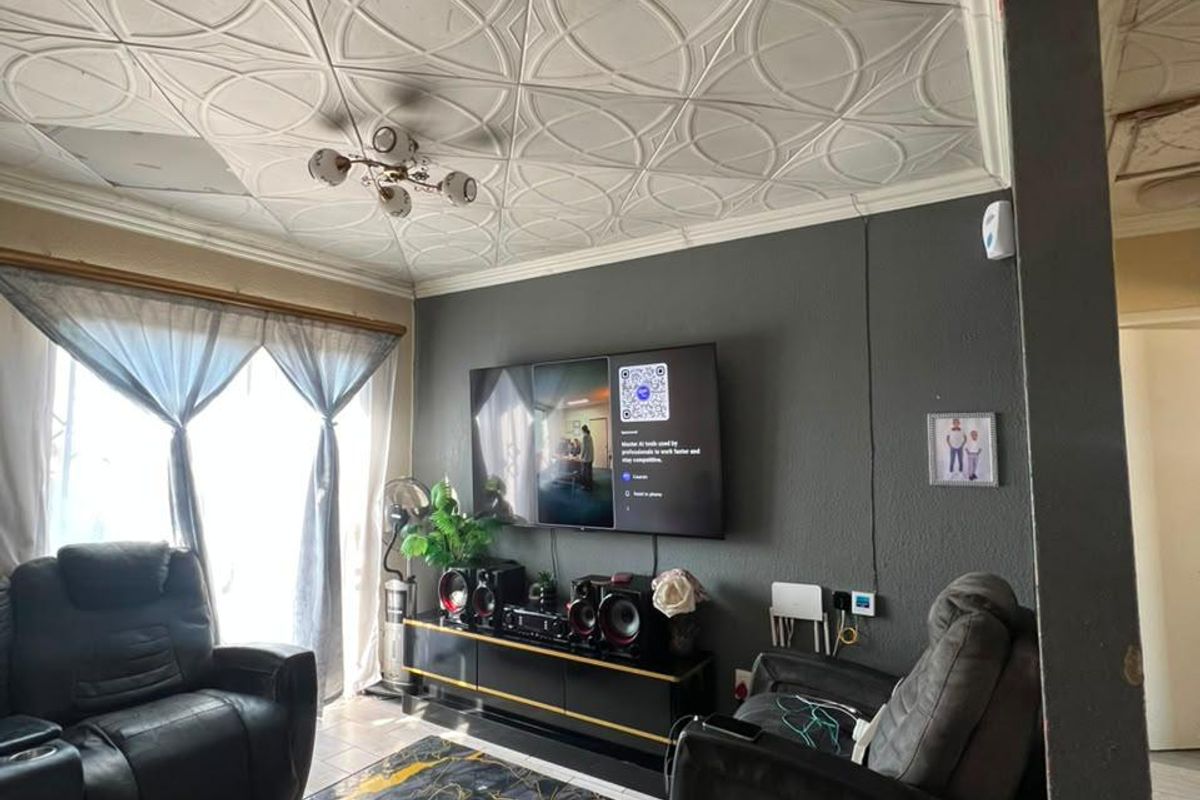 A living room featuring decorative ceiling tiles, tiled flooring, and a wall-mounted television, showing signs of wear and exposed wiring.