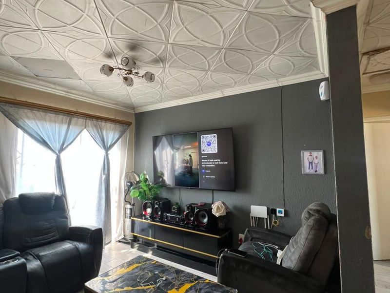 A living room featuring decorative ceiling tiles, tiled flooring, and a wall-mounted television, showing signs of wear and exposed wiring.