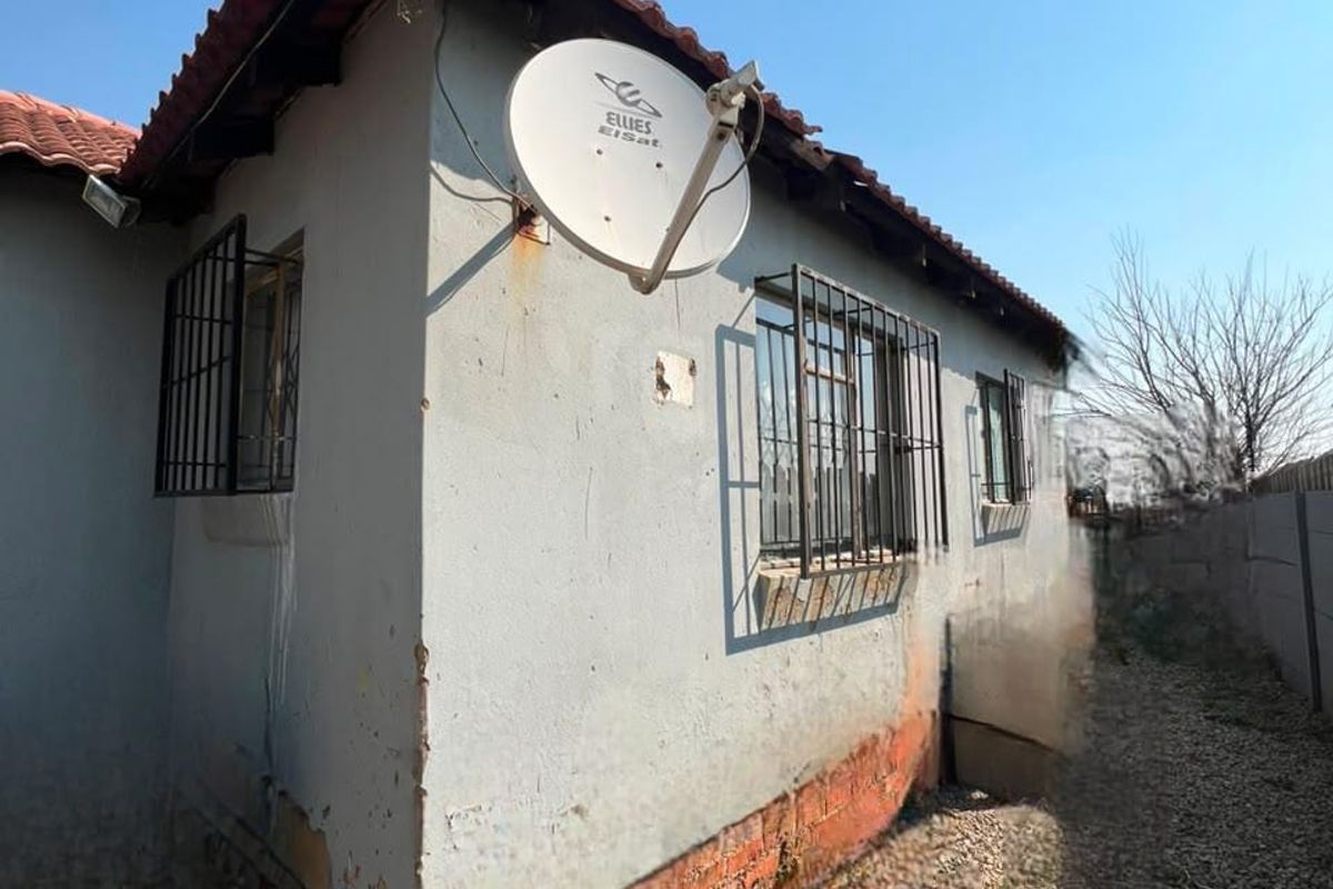 Rear exterior view of the property showing plastered brick walls, security bars on windows, and a satellite dish, with visible signs of exterior wear.