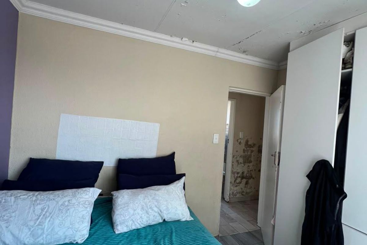 Bedroom featuring built-in wardrobe, tiled flooring, and decorative ceiling rose. The room requires significant maintenance to address ceiling and wall plaster damage.