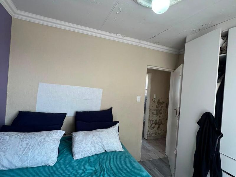 Bedroom featuring built-in wardrobe, tiled flooring, and decorative ceiling rose. The room requires significant maintenance to address ceiling and wall plaster damage.