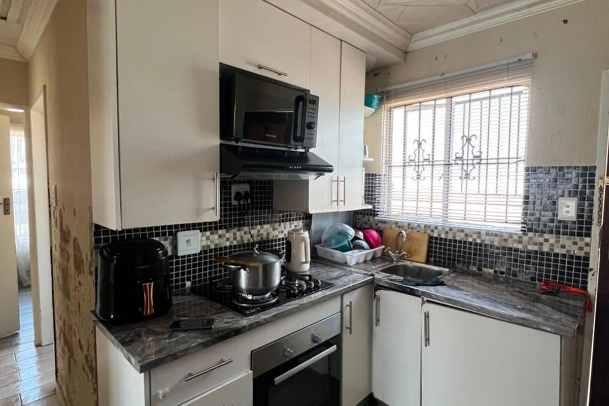 Compact kitchen featuring built-in cabinetry, integrated appliances, and tiled finishes. The space requires wall repairs and cosmetic updates to improve its overall condition.
