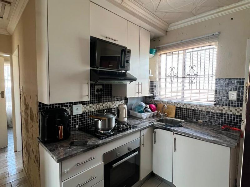 Compact kitchen featuring built-in cabinetry, integrated appliances, and tiled finishes. The space requires wall repairs and cosmetic updates to improve its overall condition.