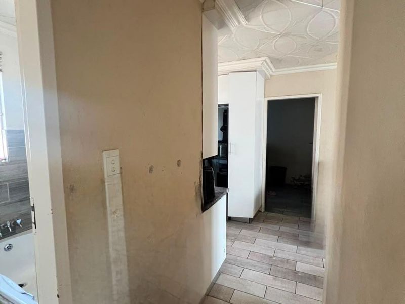 A narrow hallway featuring tiled flooring and decorative ceiling tiles, leading towards a kitchen area with built-in cabinetry.