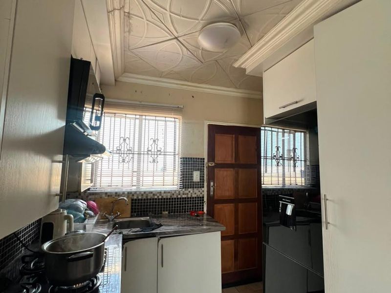 Compact kitchen featuring built-in cabinetry, gas hob, extractor fan, and decorative ceiling tiles, offering a functional layout with potential for modern updates.