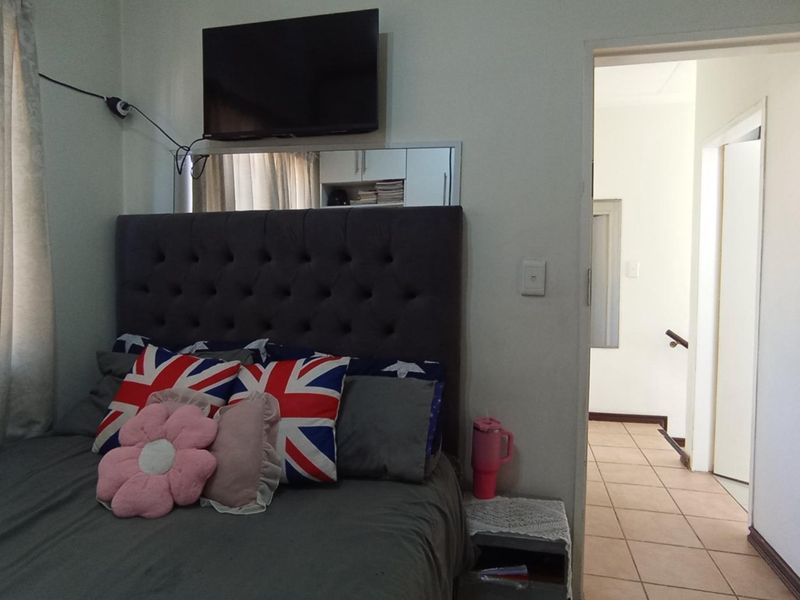 A bedroom featuring tiled flooring and a wall-mounted television, with an adjacent hallway visible through the doorway.