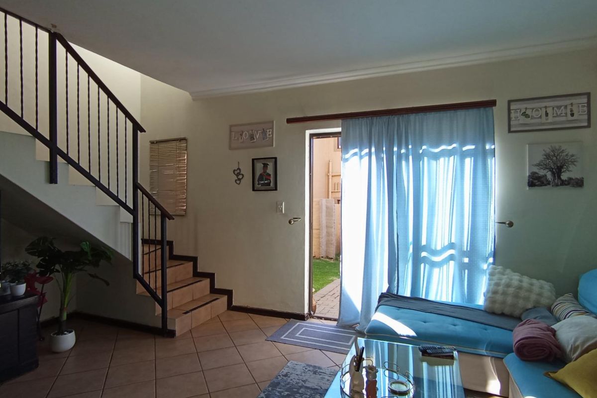 A living room featuring tiled flooring, a staircase with a metal balustrade, and a sliding door providing access to the outdoor area.