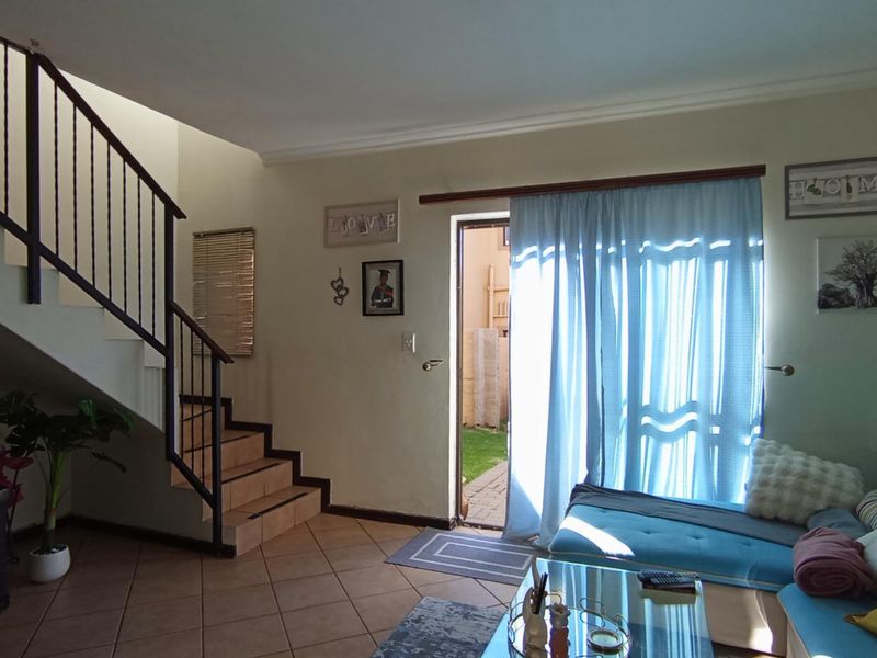 A living room featuring tiled flooring, a staircase with a metal balustrade, and a sliding door providing access to the outdoor area.