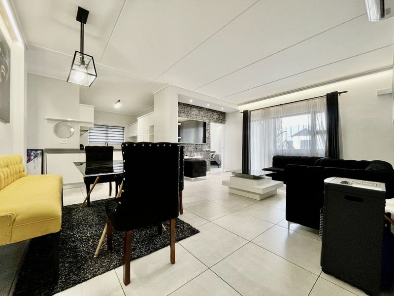 Spacious open-plan living and dining area featuring modern tiled flooring, recessed ceiling lighting, and a stylish exposed brick feature wall.