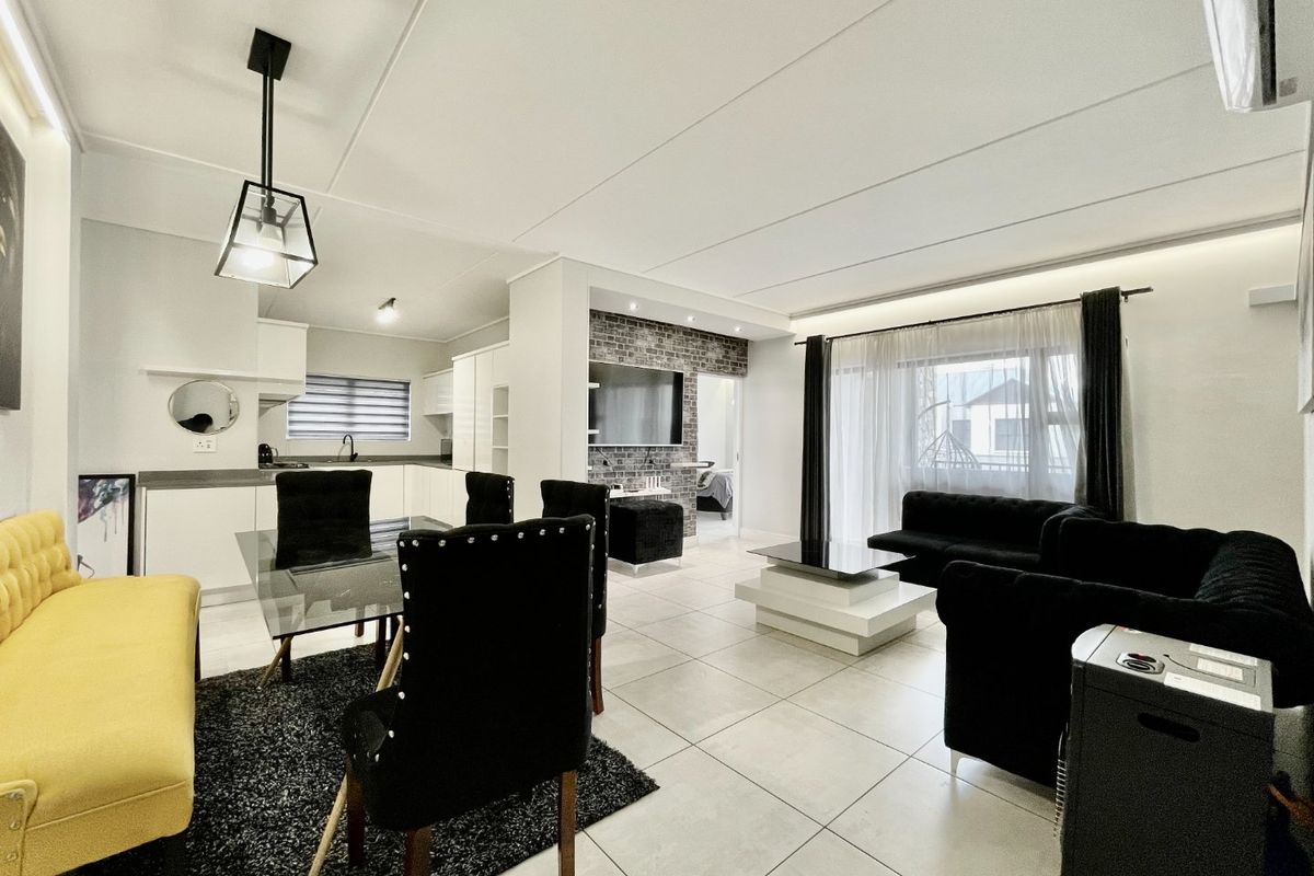 Modern open-plan living and dining area featuring tiled floors, an exposed brick feature wall, and seamless access to the balcony.
