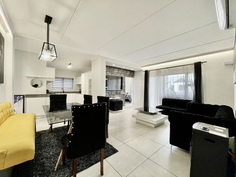 Modern open-plan living and dining area featuring tiled floors, an exposed brick feature wall, and seamless access to the balcony.
