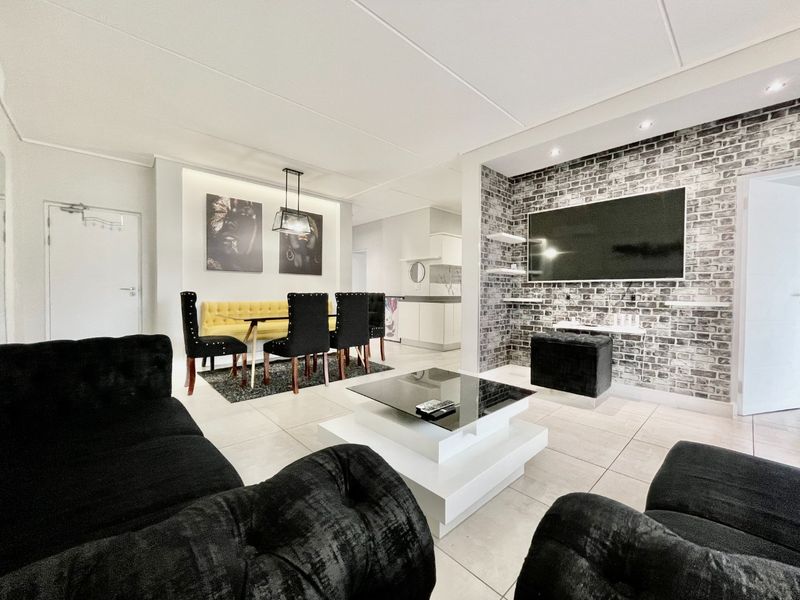 Spacious open-plan living and dining area featuring tiled flooring, recessed lighting, and a decorative brick-effect feature wall.