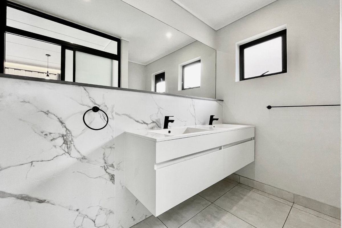 Modern bathroom featuring a sleek wall-mounted double vanity with marble-look tiling, black fixtures, and a large integrated mirror.