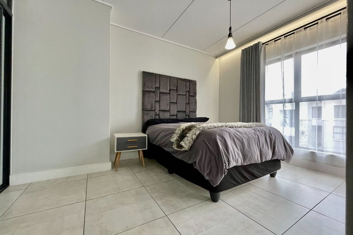 A well-maintained bedroom featuring large windows, neutral tiled flooring, and modern pendant lighting, creating a bright and comfortable living space.