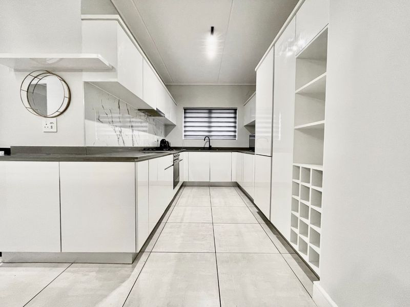 Modern galley-style kitchen featuring high-gloss white cabinetry, marble-look splashback, integrated appliances, and sleek tiled flooring.