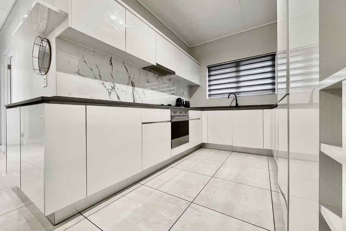 Modern kitchen featuring sleek white cabinetry, marble-look splashback, integrated oven, extractor fan, and tiled flooring.