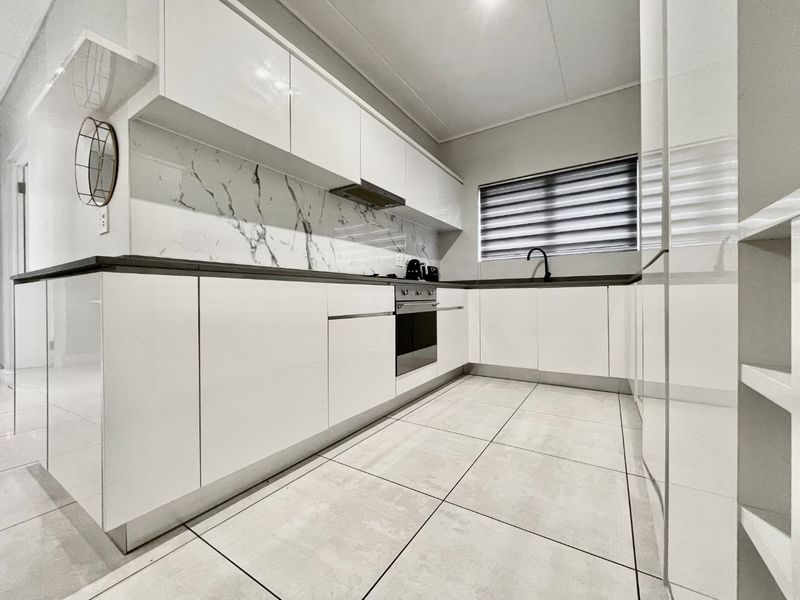 Modern kitchen featuring sleek white cabinetry, marble-look splashback, integrated oven, extractor fan, and tiled flooring.