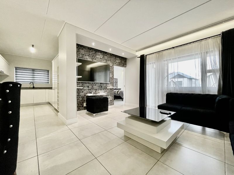Modern open-plan living area featuring a striking exposed brick feature wall, sleek tiled flooring, and a seamless transition into a contemporary kitchen space.