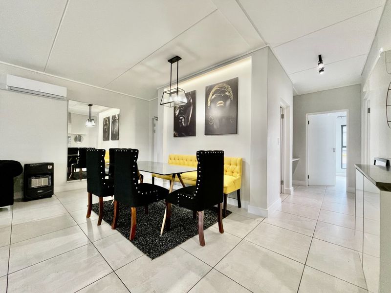 A bright and modern dining area featuring tiled flooring, recessed lighting, and a built-in wall mirror, creating an open and inviting atmosphere.