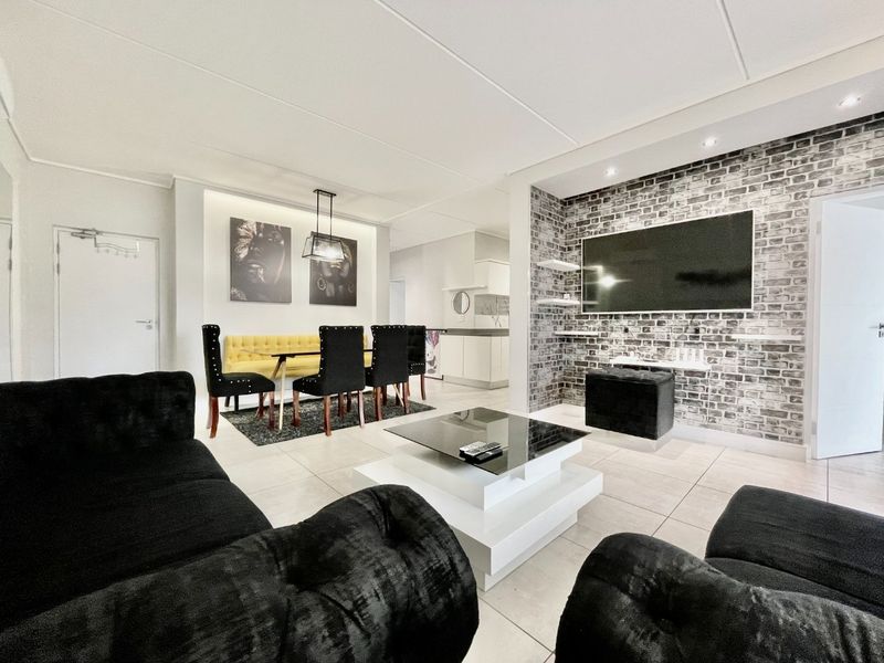 Spacious open-plan living and dining area featuring modern tiled flooring, a striking exposed brick feature wall, and integrated recessed lighting.