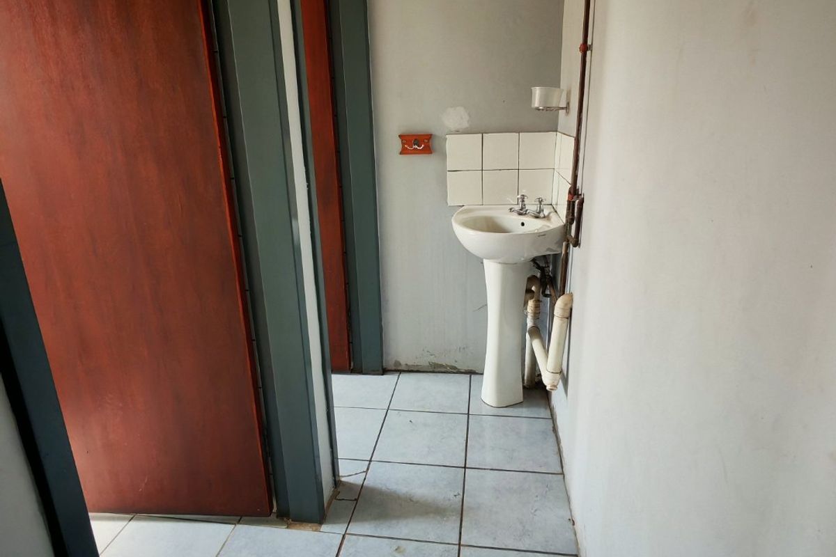 A functional industrial-style washroom area featuring a pedestal basin with exposed plumbing and tiled flooring.