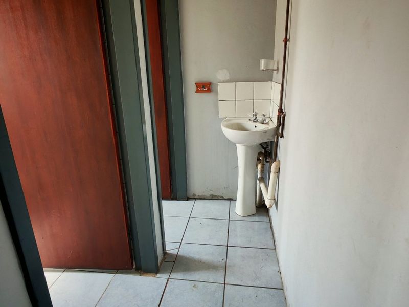 A functional industrial-style washroom area featuring a pedestal basin with exposed plumbing and tiled flooring.