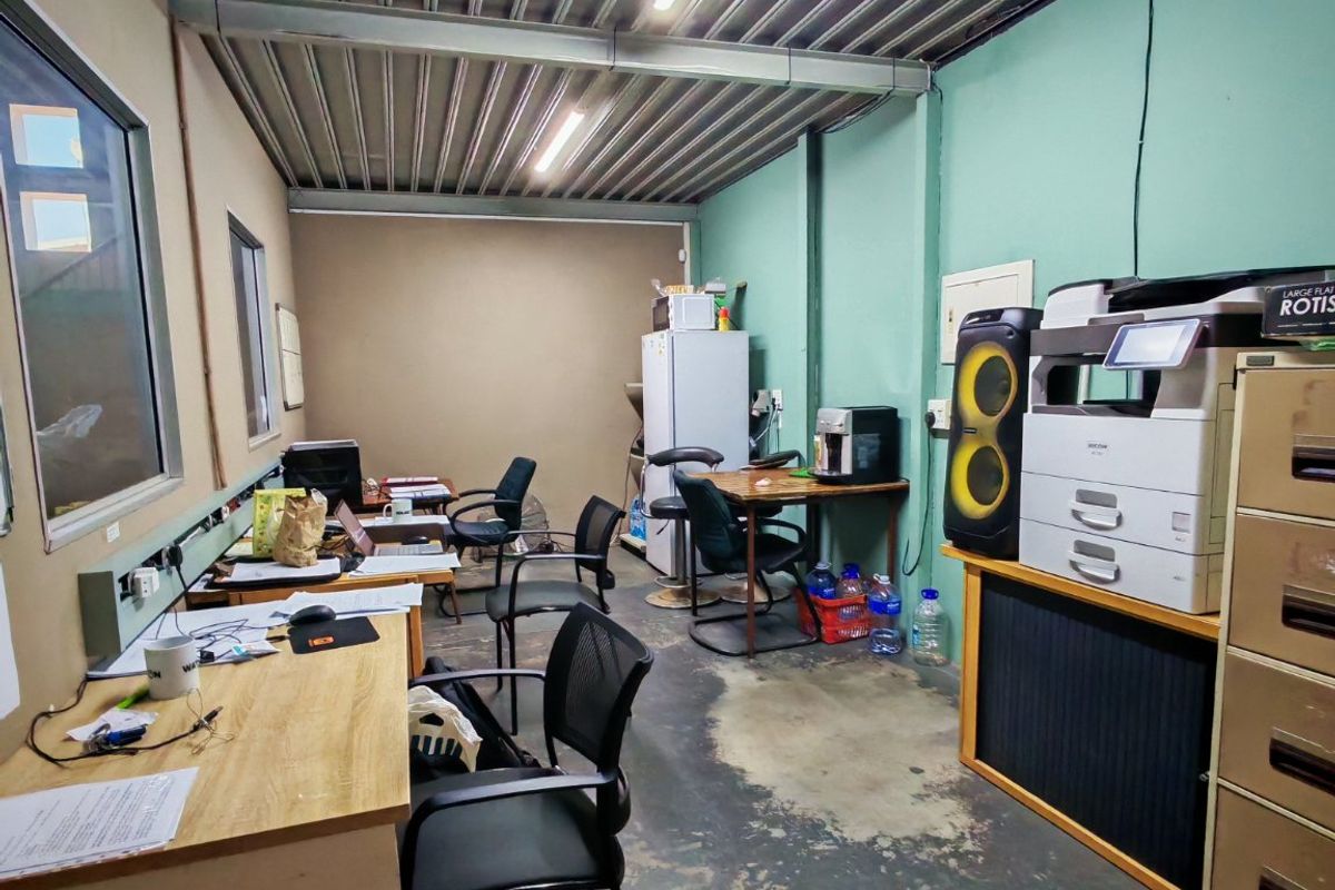 Industrial-style office space featuring exposed steel ceiling beams, corrugated metal roofing, and concrete flooring with integrated electrical trunking.