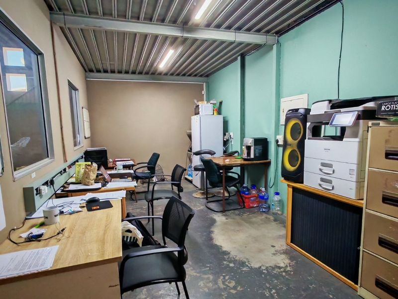 Industrial-style office space featuring exposed steel ceiling beams, corrugated metal roofing, and concrete flooring with integrated electrical trunking.