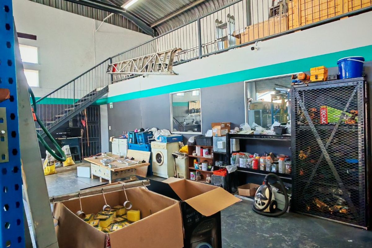 Industrial utility space featuring a mezzanine level with metal staircase, exposed steel roof structure, and functional storage area.
