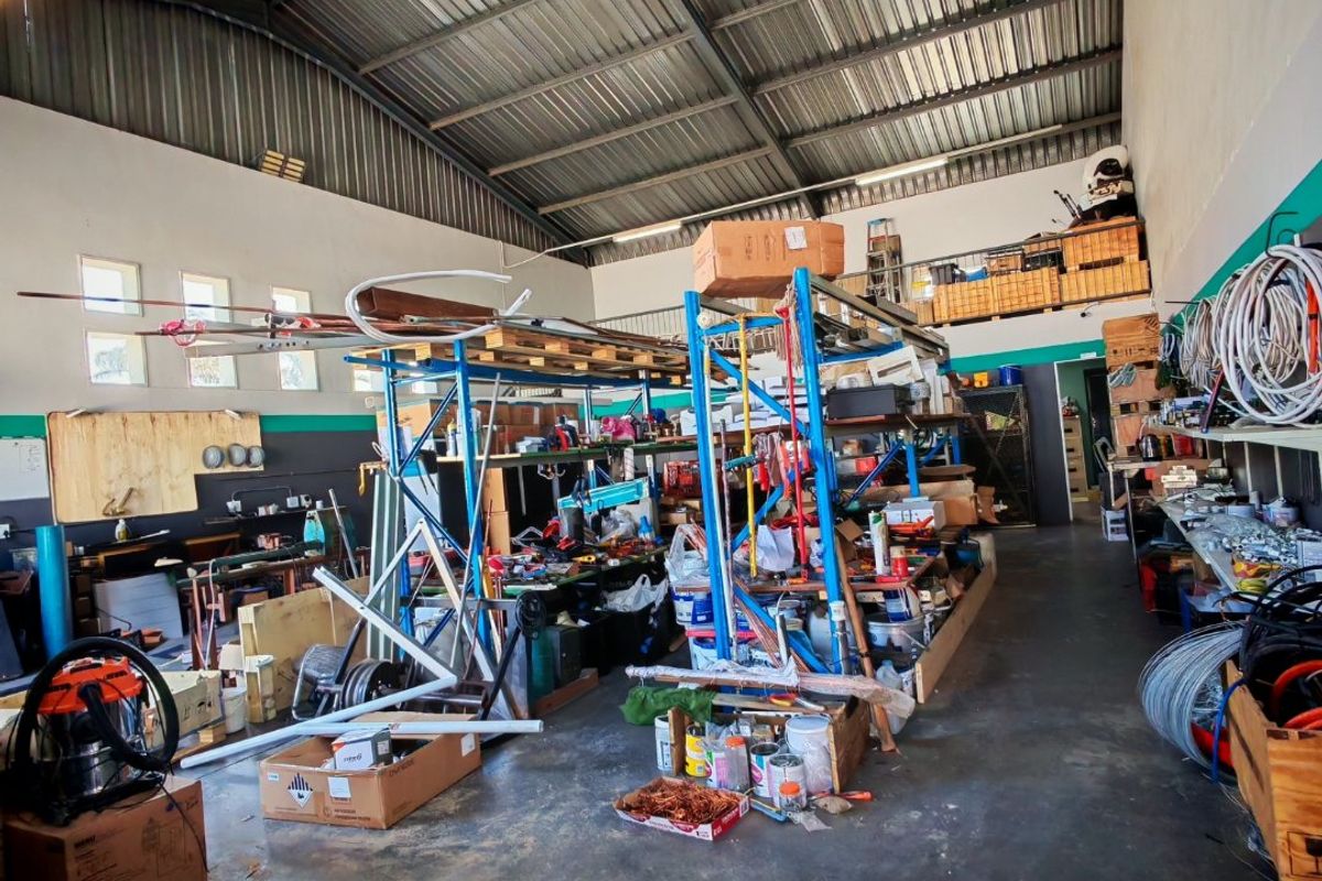 Spacious industrial utility area featuring high exposed steel roofing, concrete flooring, and integrated mezzanine storage, suitable for workshop or warehouse operations.
