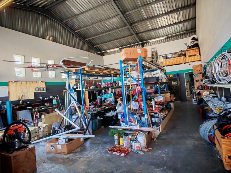 Spacious industrial utility area featuring high exposed steel roofing, concrete flooring, and integrated mezzanine storage, suitable for workshop or warehouse operations.