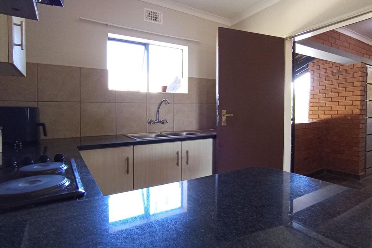 Functional kitchen featuring dark granite countertops, built-in cabinetry, a double sink, and an electric hob with a tiled backsplash.