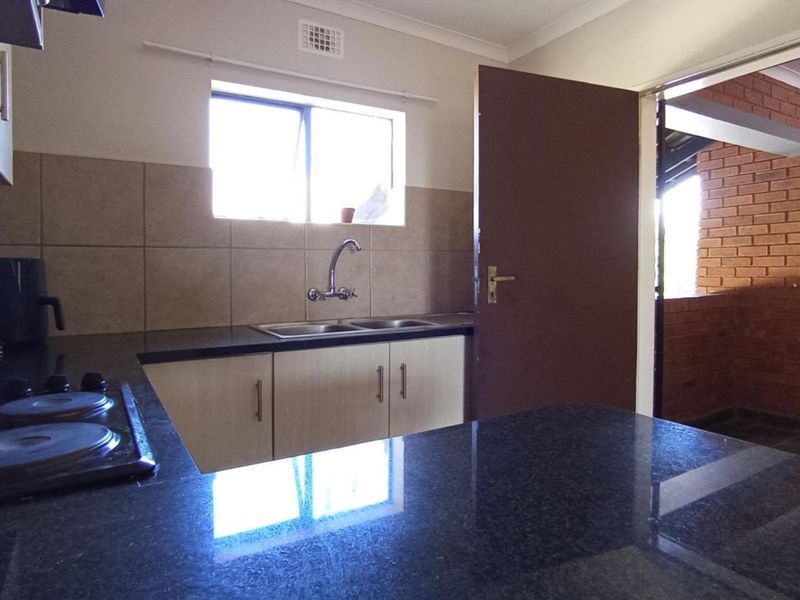 Functional kitchen featuring dark granite countertops, built-in cabinetry, a double sink, and an electric hob with a tiled backsplash.