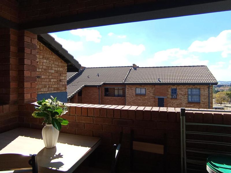 A covered balcony featuring exposed brick walls and a view overlooking the surrounding apartment complex.