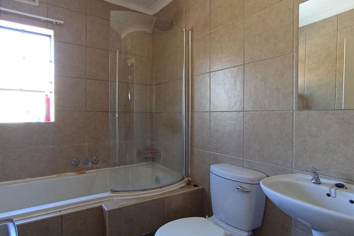 A functional bathroom featuring a bathtub with a glass shower screen, pedestal basin, and neutral wall tiling.