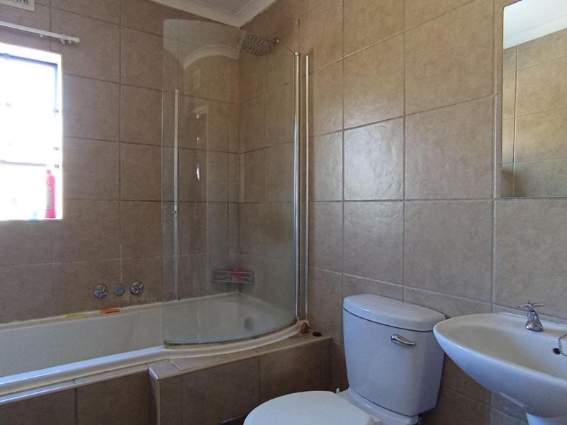 A functional bathroom featuring a bathtub with a glass shower screen, pedestal basin, and neutral wall tiling.