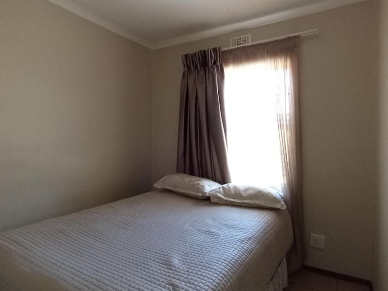 A simple bedroom featuring neutral walls, a window with curtain treatments, and standard electrical fixtures.