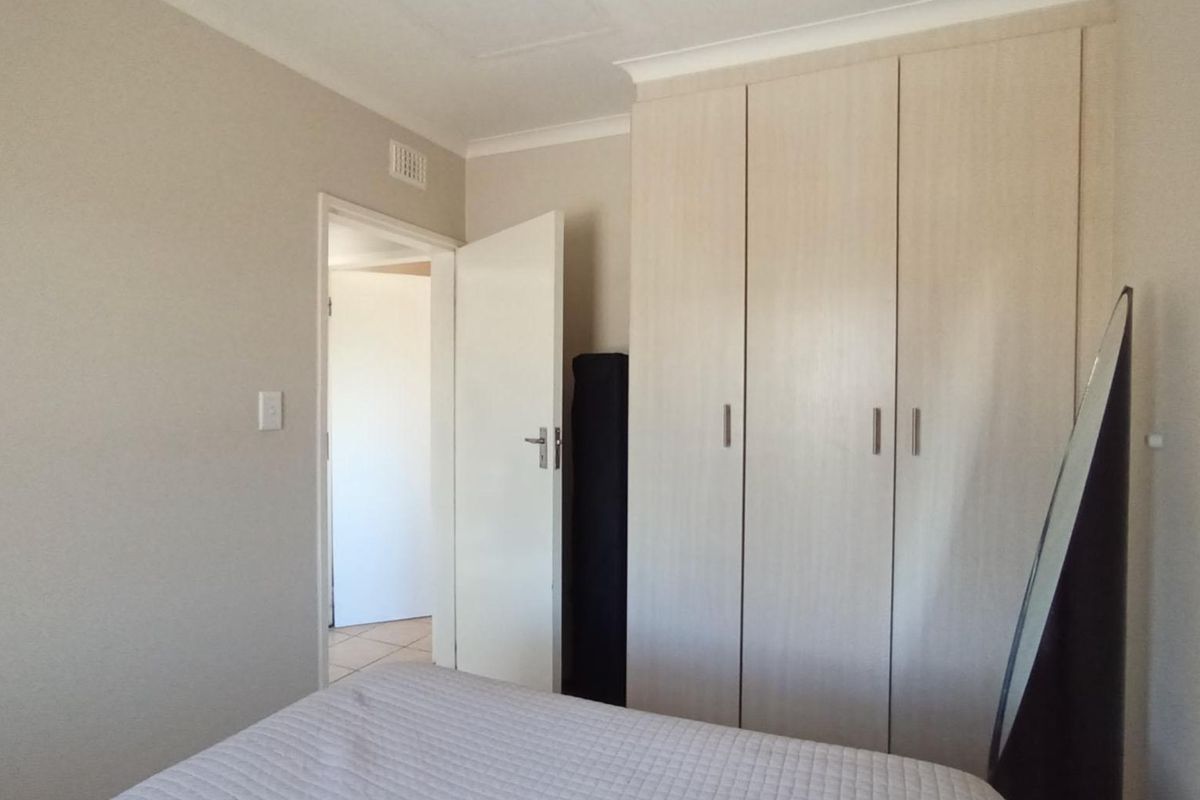 A bedroom featuring light-toned built-in wardrobes, neutral wall finishes, and a doorway leading to an adjacent space.