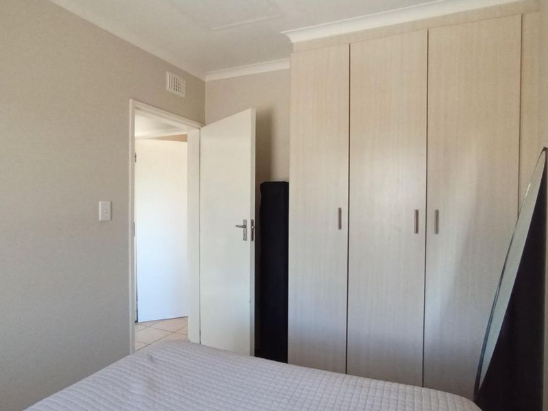 A bedroom featuring light-toned built-in wardrobes, neutral wall finishes, and a doorway leading to an adjacent space.