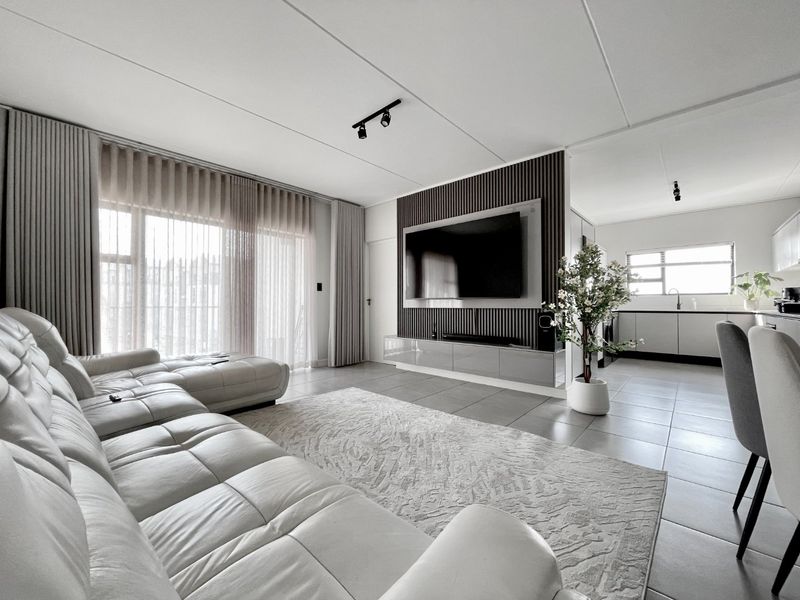 Modern open-plan living area featuring tiled floors, a stylish slatted feature wall with integrated media console, and a seamless transition to the kitchen.