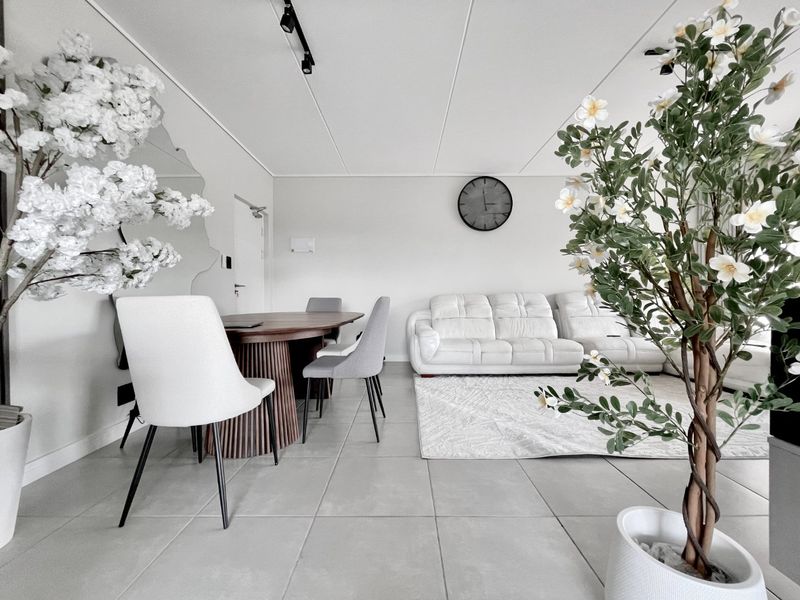 A bright open-plan living and dining area featuring neutral tiled flooring, modern track lighting, and a contemporary wall mirror.
