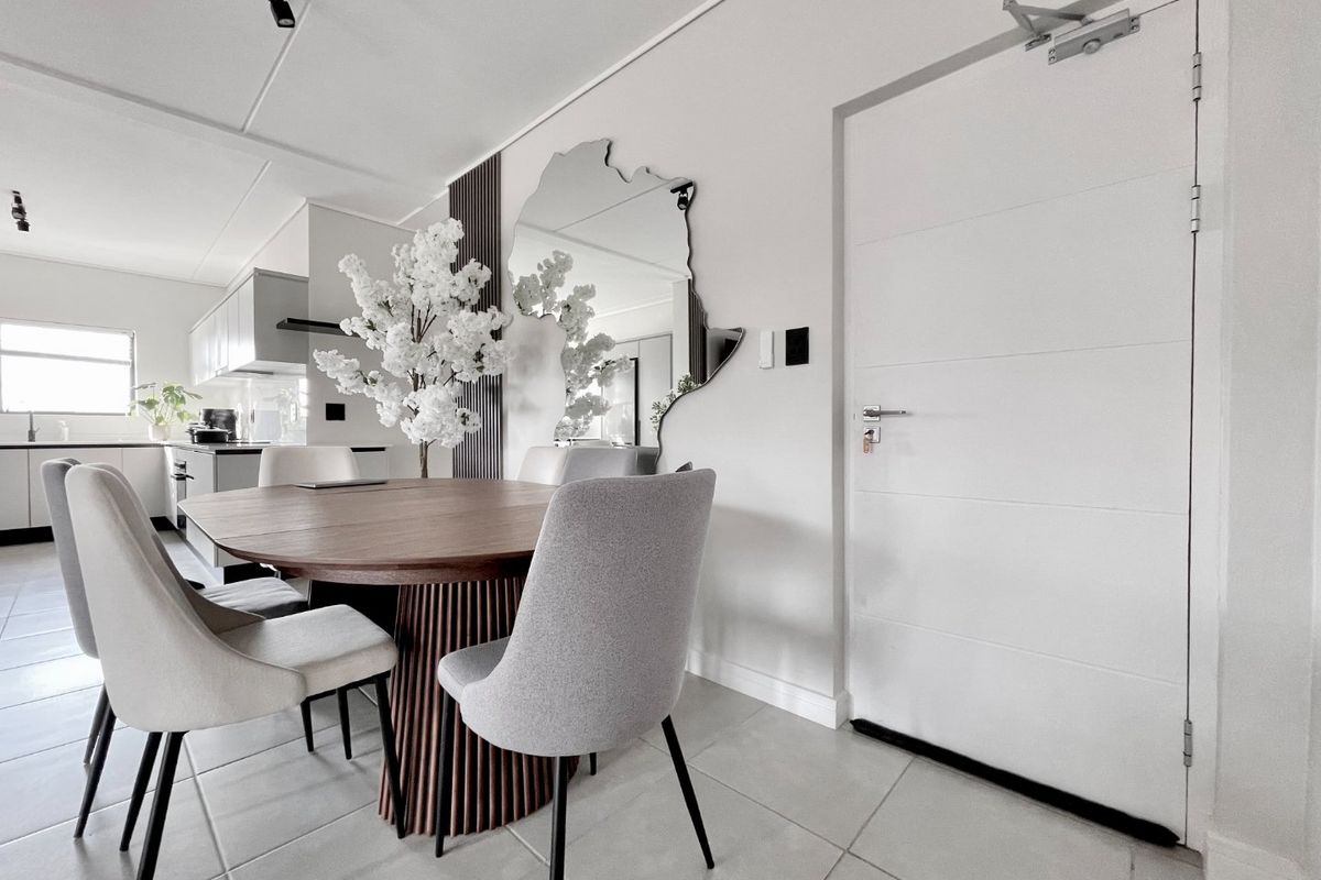 Modern open-plan dining and kitchen area featuring neutral tiled flooring, contemporary cabinetry, and a functional fire-rated entrance door.
