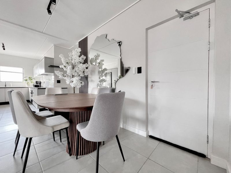 Modern open-plan dining and kitchen area featuring neutral tiled flooring, contemporary cabinetry, and a functional fire-rated entrance door.