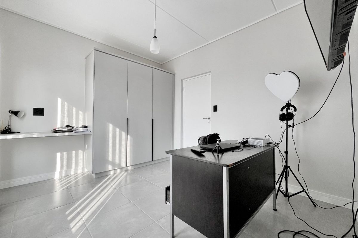 A bright bedroom featuring neutral tiled flooring, a built-in wardrobe, and a floating desk, offering a clean and functional living space.