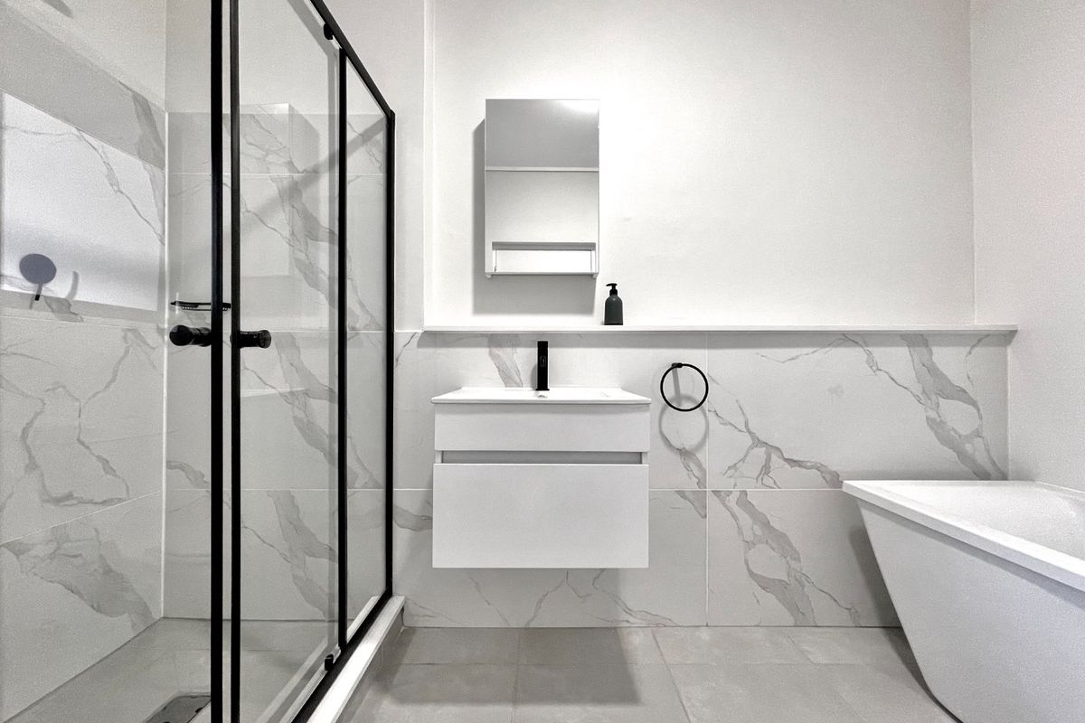 Modern bathroom featuring a walk-in shower with black-framed glass, a sleek wall-mounted vanity, and a contemporary freestanding bathtub with marble-look tiling.