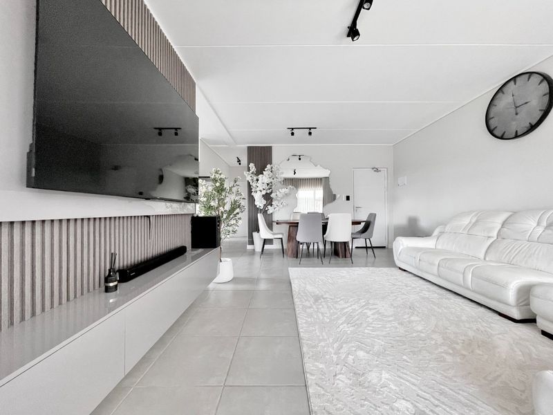 Modern open-plan living and dining area featuring sleek tiled floors, contemporary track lighting, and a stylish slatted timber feature wall with built-in media cabinetry.