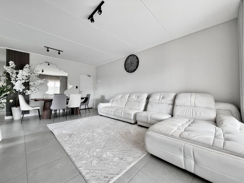 Spacious open-plan living and dining area featuring neutral tiled flooring, modern track lighting, and decorative slatted wall paneling.
